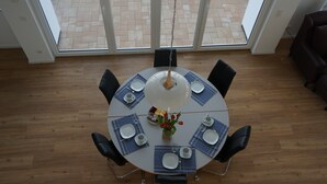 Een ronde eettafel met blauwe placematen, witte borden en een vaas rode bloemen.
