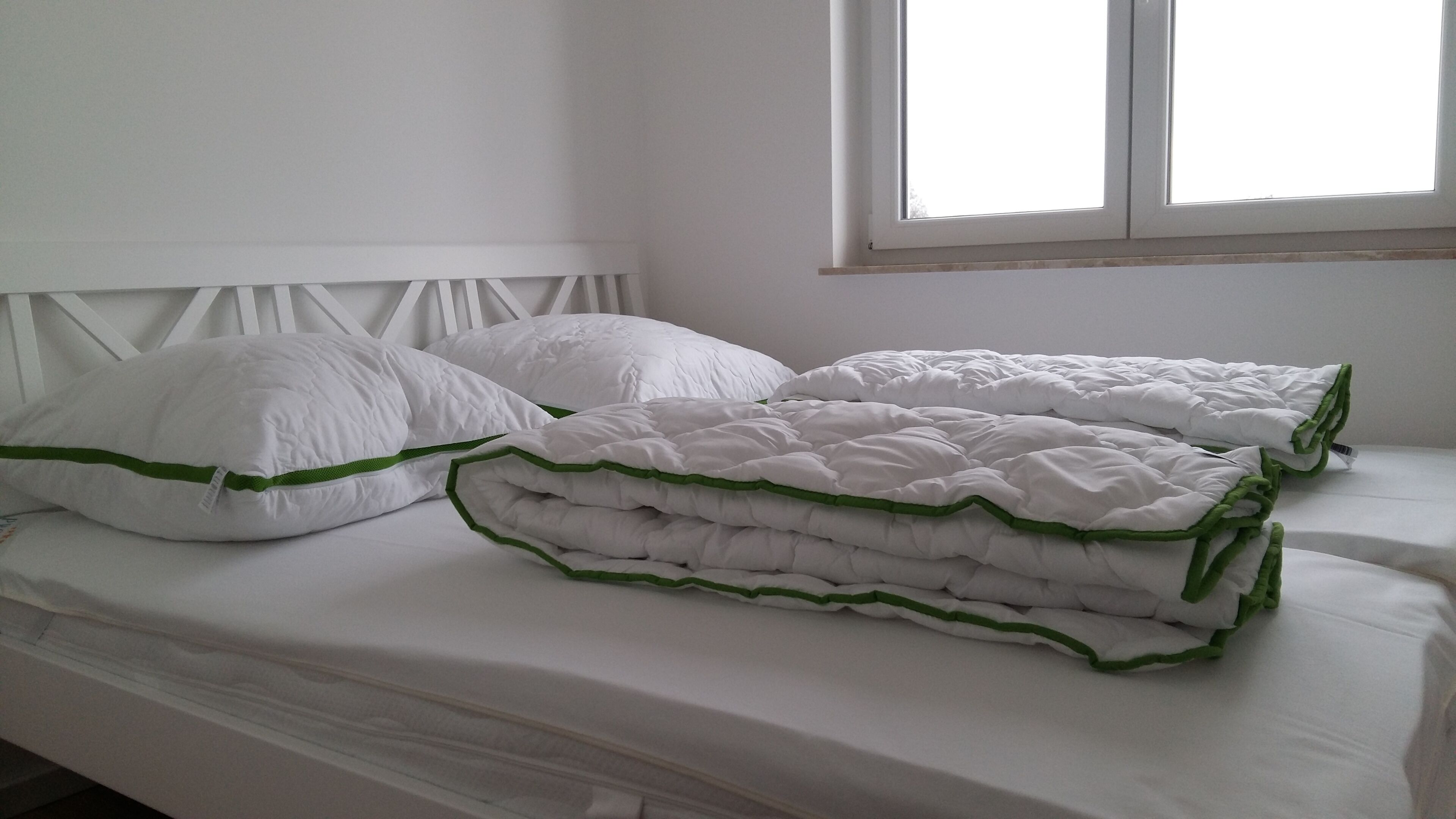 A bed with white bedding and green trim, a white headboard, and a window with natural light.