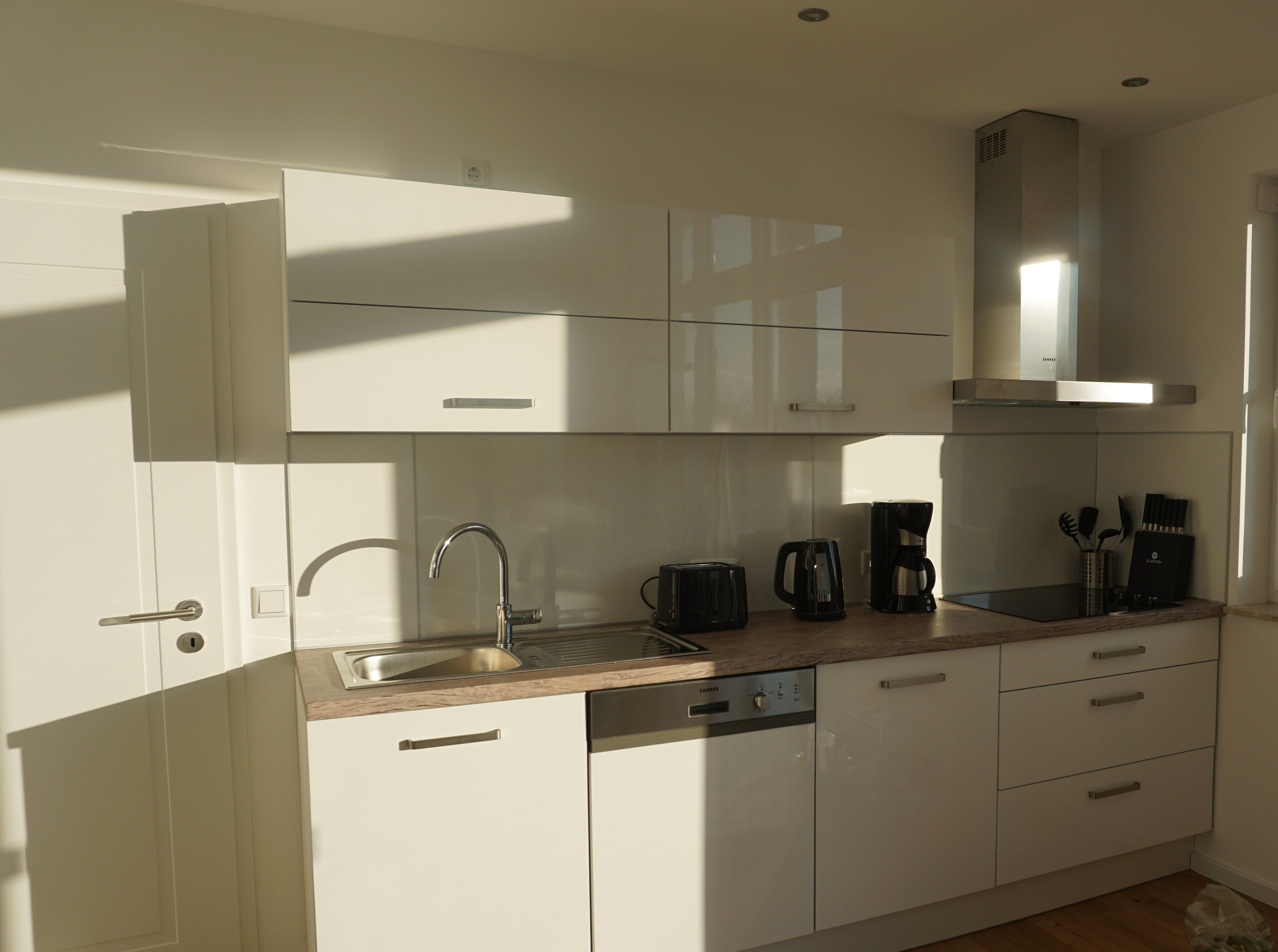 A modern kitchen with white cabinetry, a stainless steel sink, a dishwasher, and a coffee maker.