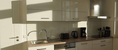 A modern kitchen with white cabinetry, a stainless steel sink, a dishwasher, and a coffee maker.