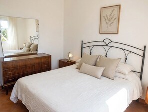 A bedroom with a bed, a dresser, a nightstand, a lamp, a mirror, and a framed botanical print on the wall. - panoramica casa con piscina privata (siena)