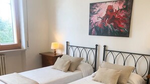 Ein Schlafzimmer mit zwei Betten, einem Nachttisch mit Lampe, einem Fenster und einem Gemälde an der Wand.
