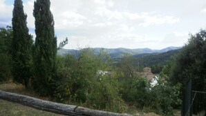 Une vue d’un paysage rural, avec une clôture en bois au premier plan, un bâtiment situé au loin et, en arrière-plan, des collines et des arbres.
