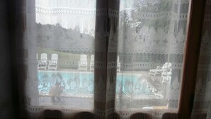 Una ventana con cortina estampada, vista a una piscina y un edificio al fondo.