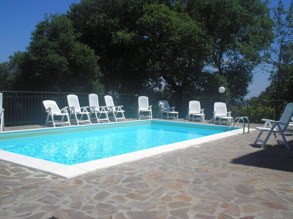A swimming pool with white lounge chairs and a stone patio.