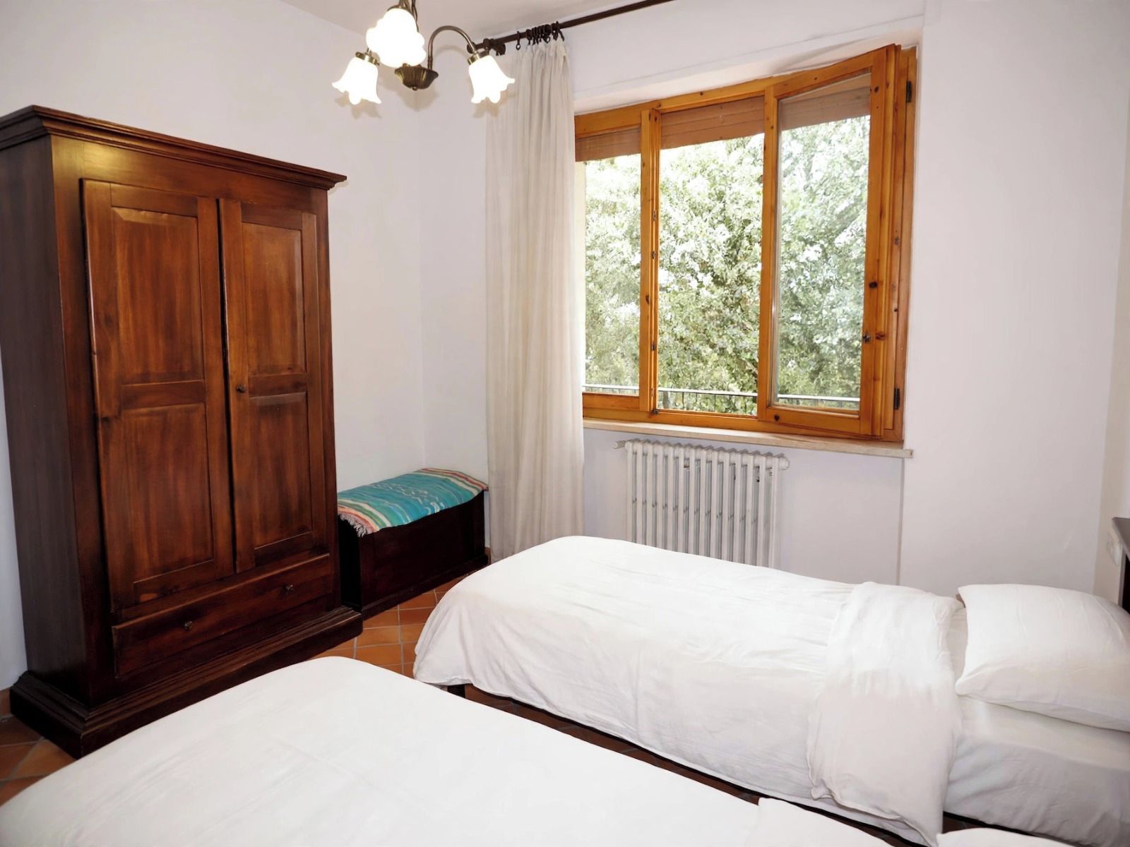Un dormitorio con dos camas, un armario, una ventana con vistas a árboles y un radiador.