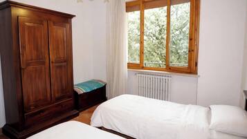 Un dormitorio con dos camas, un armario, una ventana con vistas a árboles y un radiador.