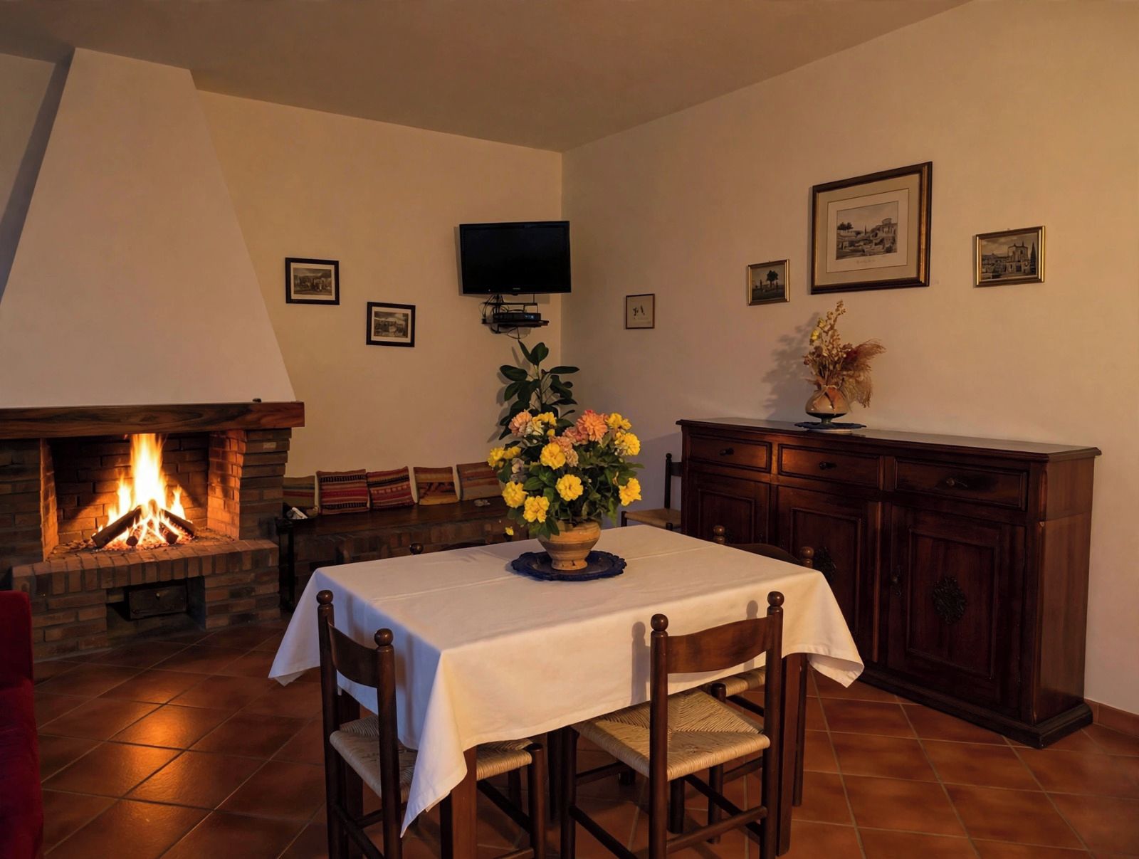 A dining area with a fireplace, a table set for two, and a television mounted on the wall.