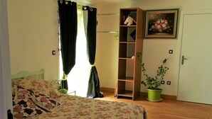 Een slaapkamer met een bloemenbedekker, een houten boekenkast, een potplant en een deur met een schilderij.