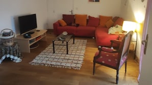 Een woonkamer met een rode bank, een salontafel, een televisietoestel en een lamp.