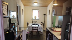 Een smalle keuken met een eethoek, houten plafond en een raam met gordijnen.