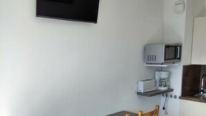 A small kitchen with a wooden table and chairs, a microwave, a coffee maker, and a TV mounted on the wall. - Apartment facing south, magnificent views, secure private garage (Font-Romeu-Odeillo-Via)