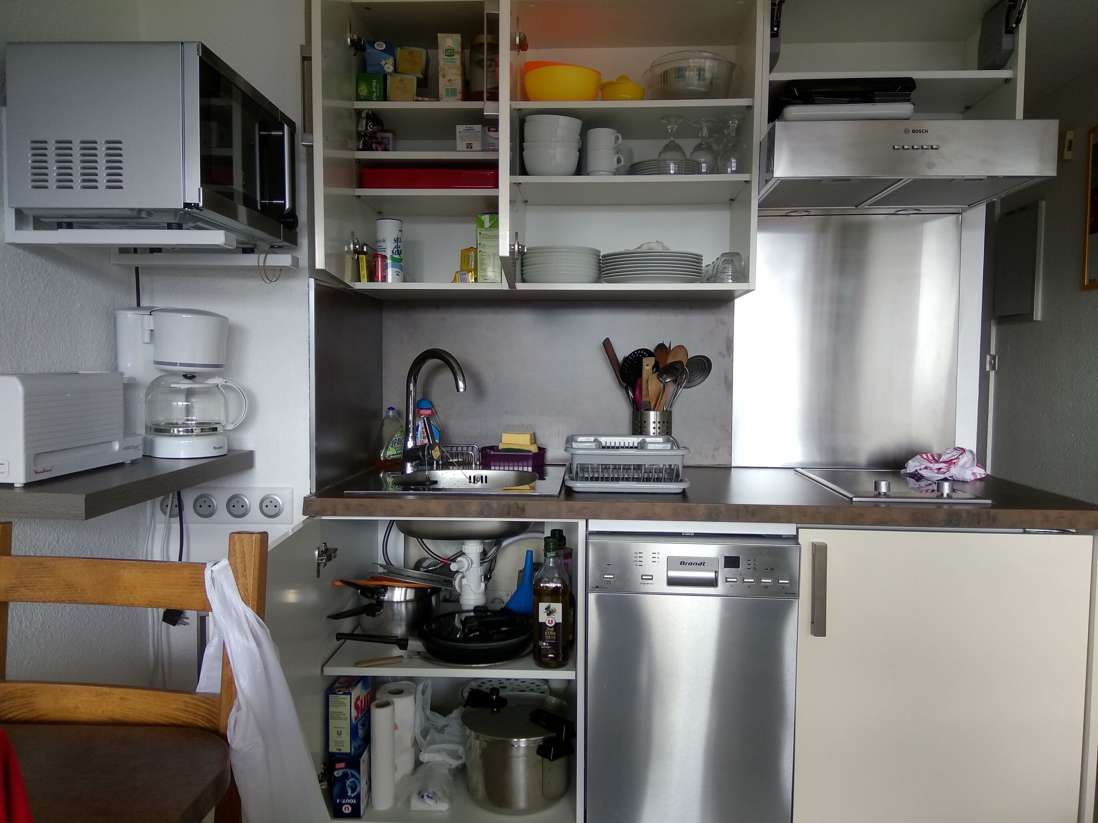 Een compacte keuken met een ingebouwde magnetron, een koffiezetapparaat, een spoelbak en een roestvrijstalen koelkast.