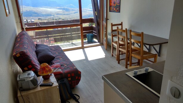 A cozy living area with a sofa, a small desk with a computer, and a view of a balcony. - Apartment facing south, magnificent views, secure private garage (Font-Romeu-Odeillo-Via)