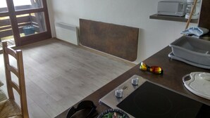 A kitchen with a microwave, a coffee maker, and a toaster. There is a chair and a table with a plate and a bowl on it. - Apartment facing south, magnificent views, secure private garage (Font-Romeu-Odeillo-Via)