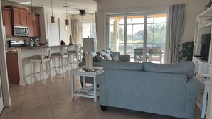 Un soggiorno moderno con un divano grigio, un angolo cottura con pensili in legno e un forno a microonde, e un'area pranzo con sedie in vimini.
