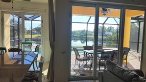 Una stanza con una porta in vetro che si apre su un patio esterno con tavolo, sedie e vista su un lago.