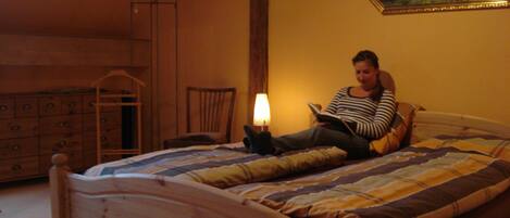 A person sitting on a bed in a room with a wooden dresser and a chair.