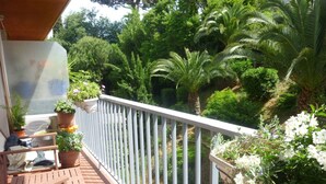 Een balkon met een witte reling, plantenbakken en een houten stoel.