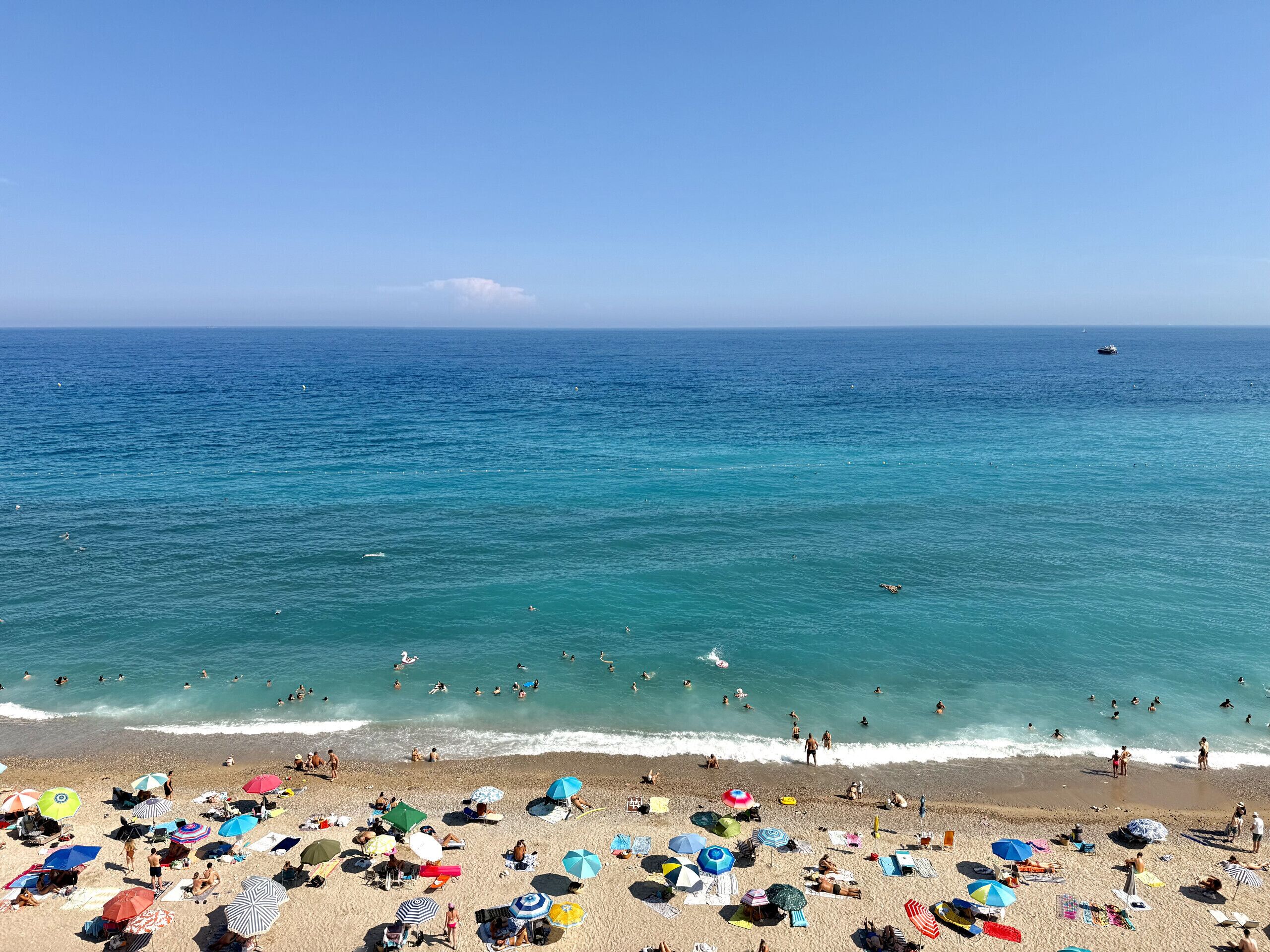 Una spiaggia con persone che nuotano e prendono il sole, ombrelloni e una barca nell'acqua.