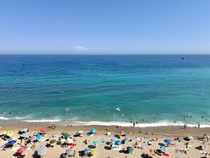 Een strand met mensen die zwemmen en zonnebaden, parasols en een boot in het water.