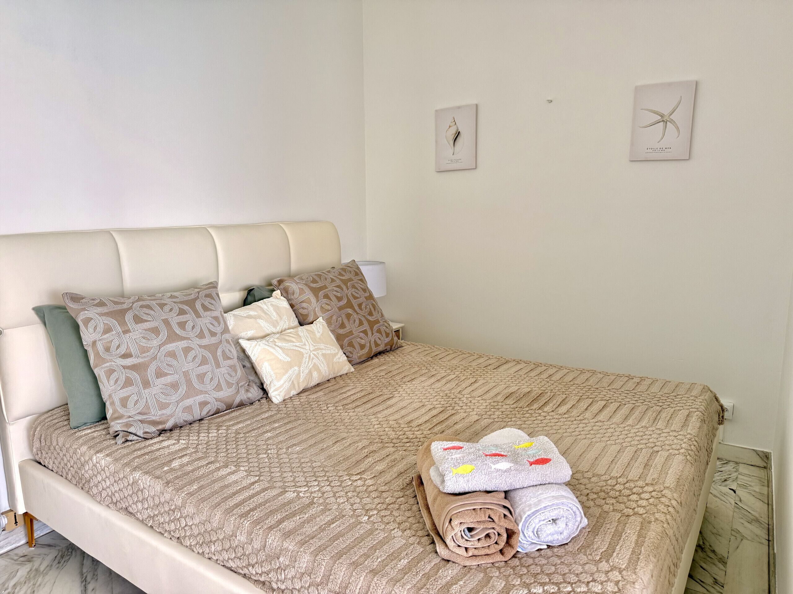 Un letto rifatto con cuscini decorati, un asciugamano arrotolato e un asciugamano piegato su un letto con pavimento in marmo.