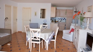 Een eethoek met een tafel en stoelen, een bank, een televisie en een keuken op de achtergrond.