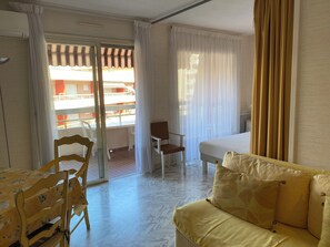 Ein Hotelzimmer mit Bett, einer Couch, einem Esstisch und einem Stuhl. Es gibt einen Balkon mit Blick nach draußen.