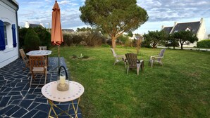 Un patio exterior con una mesa redonda y sillas, una sombrilla pequeña y un árbol.