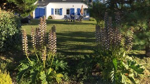 Una casa con jardín, césped y un patio con sillas y una mesa.