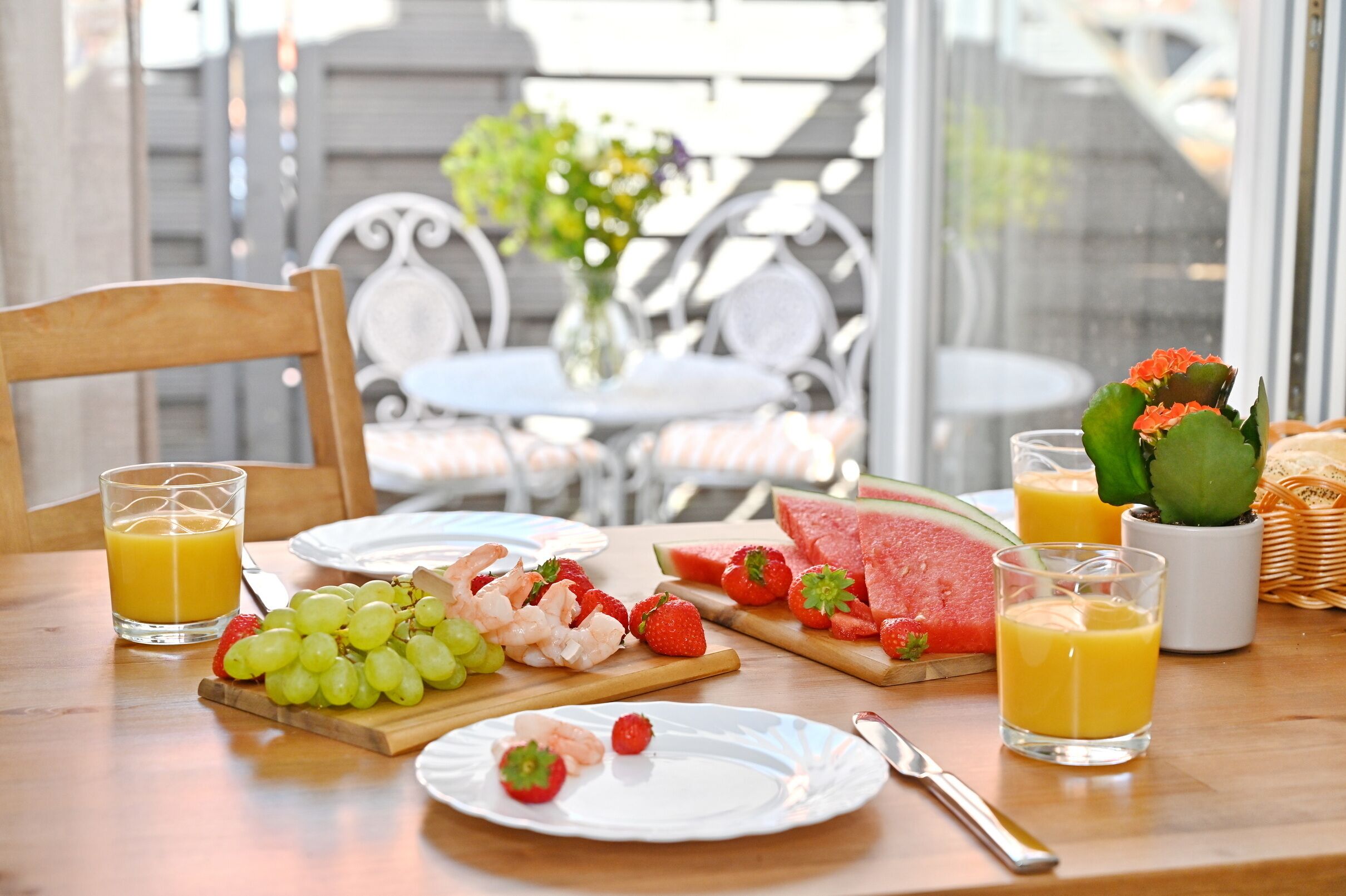 A breakfast table with plates of fruit, shrimp, and watermelon, along with glasses of orange juice.