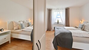 Une chambre avec deux lits, une table de chevet, une commode et une fenêtre avec des rideaux.