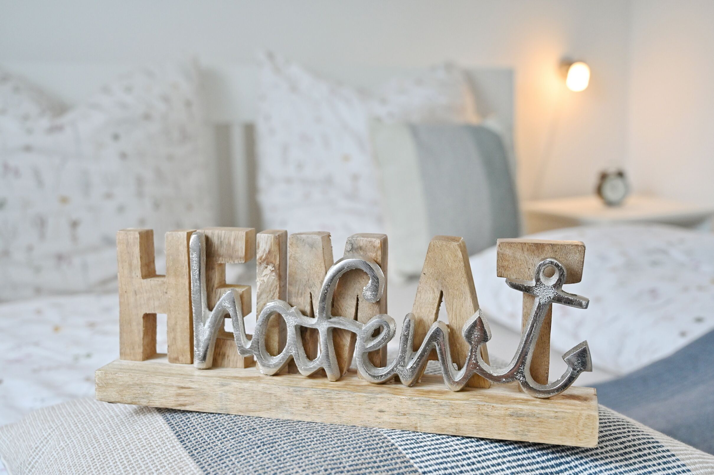 A wooden sign with the word "HOME" on a bed with a white and gray patterned bedspread.