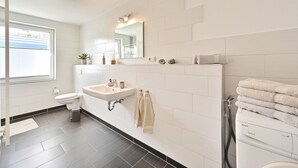 Une salle de bain moderne avec des toilettes, un lavabo et une douche. Un miroir se trouve au-dessus du lavabo et une fenêtre est située à gauche.