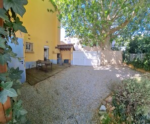 Un patio couvert avec une table et des chaises, un barbecue et un portail blanc.