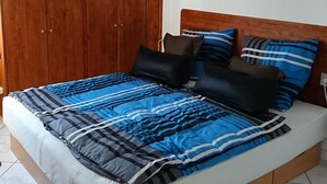 A bedroom with a bed, wooden wardrobe, and an air conditioning unit.