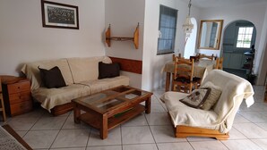 A living room with a sofa, a coffee table, a chair, a wooden side table, a wall-mounted shelf, and a chandelier.