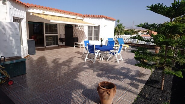 A covered patio area with a table and chairs, a small potted plant, and a tiled floor.
