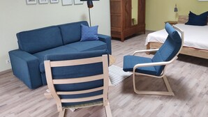 A room with a blue sofa, a wooden chair, a bed, a wardrobe, and several framed pictures on the wall.