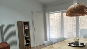 A dining area with a wooden table, white chairs, a bookshelf, and a radiator.