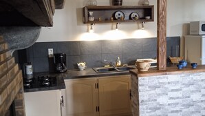 A kitchen with a wooden beam ceiling, a built-in stove, a sink, and a shelf with decorative items.