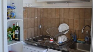Kompakti keittiö, jossa on valkoiset kaapit, Bosch-astianpesukone, pesuallas ja laatoitettu välitila.