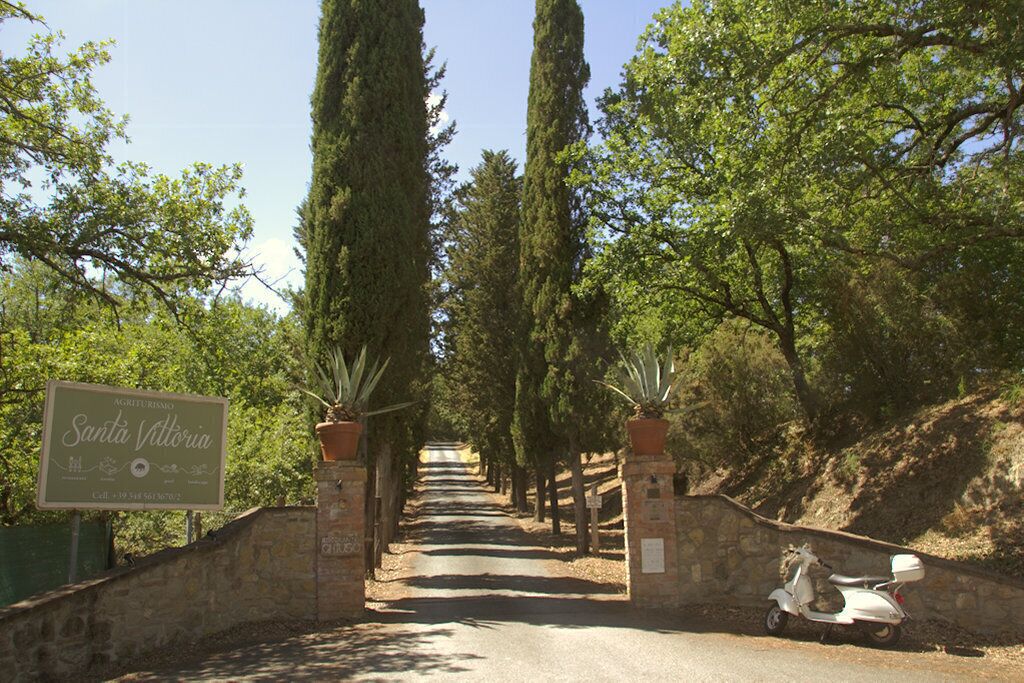 A paved pathway leading to a gated entrance with a sign for Santa Vittoria.