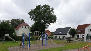 Ein Spielplatz mit diversen Geräten, umgeben von Rasenflächen und Wohngebäuden.