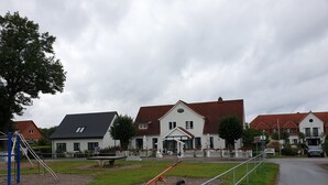 Ein Spielplatz mit einer Wippe und einer Schaukel, umgeben von einem weißen Zaun und einer Rasenfläche.