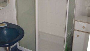 Een badkamer met een douche met glazen wand, een blauwe wastafel en een wit kastje met lades.