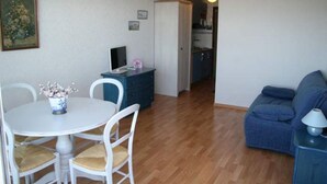 Een gezellige, compacte leefruimte met een eettafel, stoelen, een bank en een keukenhoek.