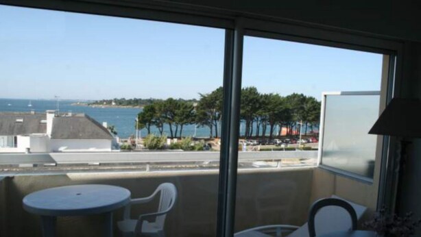 Een balkon met uitzicht op zee en bomen, een ronde tafel en twee stoelen.