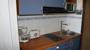 Een kleine keuken met een magnetron, broodrooster en koffiezetapparaat op het aanrecht, een spoelbak en blauwe kastjes.