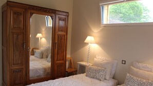 Un dormitorio con un amplio armario de madera, dos mesitas de noche con lámparas, una cama con almohadas estampadas y una ventana con vistas a árboles.